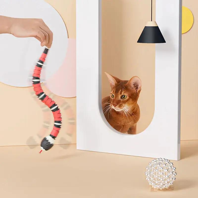 Interactive USB-rechargeable cat toy snake with smart sensing; two toys, red/black striped snake and silver lattice ball, with a curious cat.