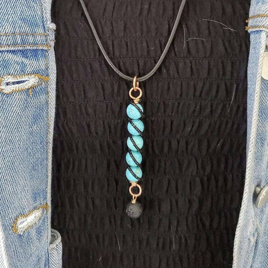 Necklace with a copper ring at the top, a vertical strand of turquoise beads, and a lava rock charm on a black cord