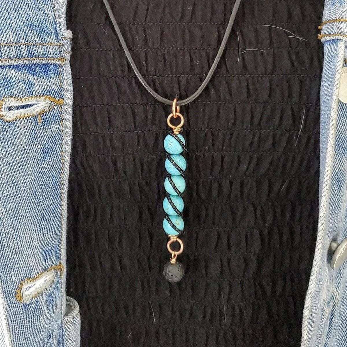 Necklace with a copper ring at the top, a vertical strand of turquoise beads, and a lava rock charm on a black cord