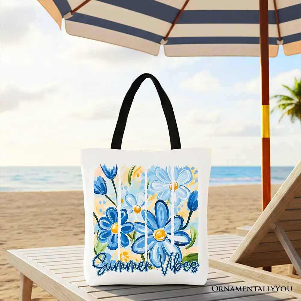Summer Vibes tote bag by OrnamentallyYou on the beach; white tote with blue brushstroke flowers and black handles.